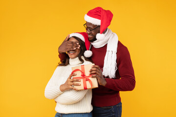 Black Man Surprising Wife With Christmas Gift Covering Eyes, Studio