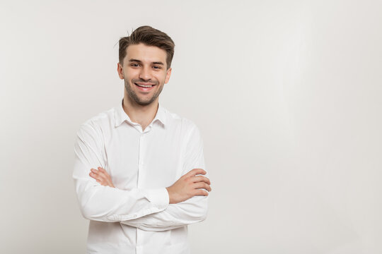 Image of happy smiling brunette man wearing white shirt smiling at camera with hands crossed on chest isolated over white background