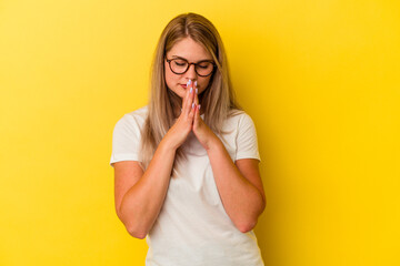 Young russian woman isolated on yellow background praying, showing devotion, religious person looking for divine inspiration.