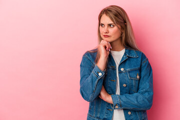 Young russian woman isolated on pink background looking sideways with doubtful and skeptical expression.