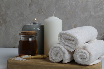 Fototapeta na wymiar Spa relaxation home care. White towels candle oil for massage lie on a wooden tray on a gray background