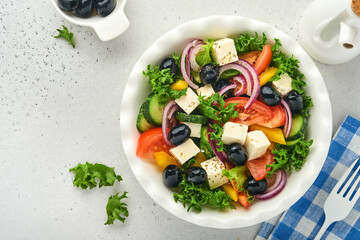 Traditional Greek salad of fresh cucumber, tomato, sweet pepper, lettuce, red onion, feta cheese and olives with olive oil on white plate. Healthy food, top view.