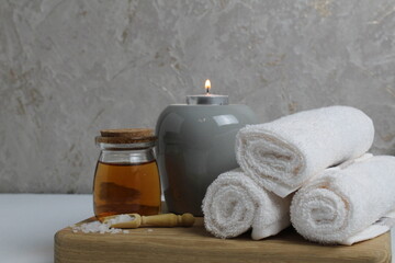 Obraz na płótnie Canvas Spa relaxation home care. White towels candle oil for massage lie on a wooden tray on a gray background
