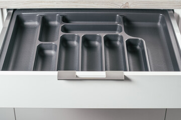 Empty open drawer of white kitchen set with black cutlery organizer tray. Storage organization system