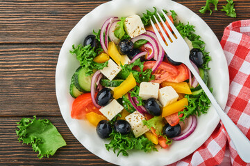 Traditional Greek salad of fresh cucumber, tomato, sweet pepper, lettuce, red onion, feta cheese and olives with olive oil on white plate. Healthy food, top view.