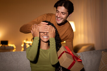 Obraz premium Boyfriend Surprising Girlfriend With Gift Closing Her Eyes At Home