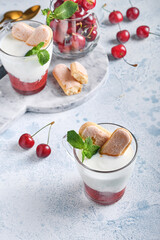 Summer cherry puff pastry with savoiardi cookies and cream cheese in glass on light grey background. Traditional tiramisu cake with fresh berries. Selective focus.
