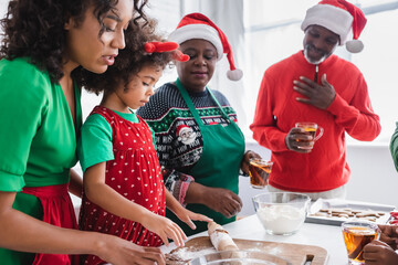pleased african american grandparents looking at granddaughter preparing christmas cookies with mother
