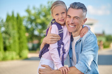 Cheerful dad and daughter hugging on walk