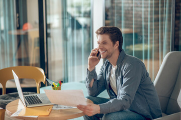 Joyful man at workplace talking on smartphone