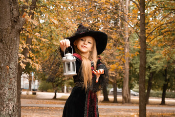 a little girl in a witch costume with a flashlight in her hands contorts on Halloween