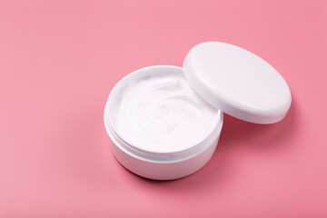 Cosmetic cream background. White cosmetic cream for skin and body in an open white jar on a pink empty background.