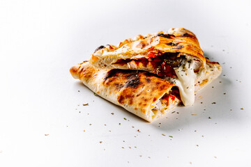 calzone pizza folded in half with meat, vegetables and cheese on a white background