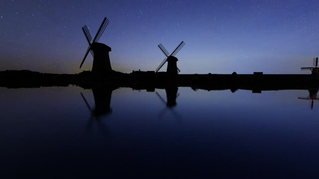 Silhouettes of three windmills on a canal during nighttime
