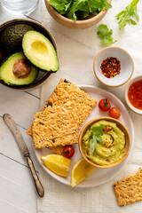 Lifestyle image of guacamole and crispy bread over wooden rustic white table, top view, healthy food concept