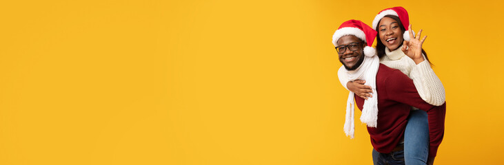 Black Man Carrying Woman Piggyback Wearing Santa Hats, Yellow Background