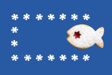 Linzer cookie in a shape of fish in a frame from snowflakes, isolated on blue background. Romantic Christmas greeting card, copy space for text