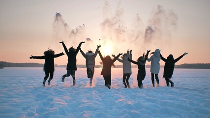 A group of girls friends are throwing snow up at sunset.