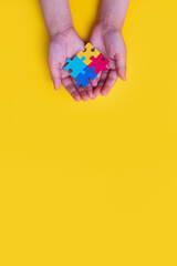 World autism awareness day. The hands of a small child holding colorful puzzles on yellow...