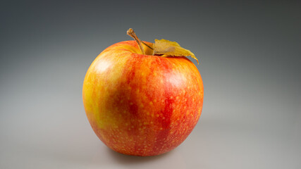 Red apple with dry leaf lies on a gray background.