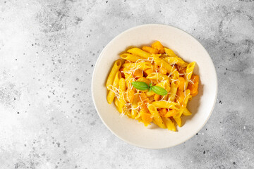 Neapolitan pasta penne rigate with pumpkin in a ceramic plate on a light gray culinary background top view with copyspace. Traditional Italian cuisine	
