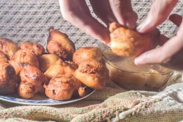 brazilian sweet called "bolinho de chuva" rain dumpling, or Fritter, in a natural home environment copy space and hands holding a dumpling, a pot with a milk candy on the side to accompany