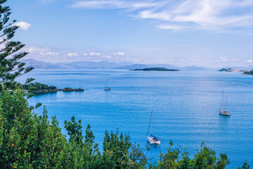 Beautiful summer landscape with sea bay with clear calm water, green trees, mountains on the horizon and clouds on blue sky.