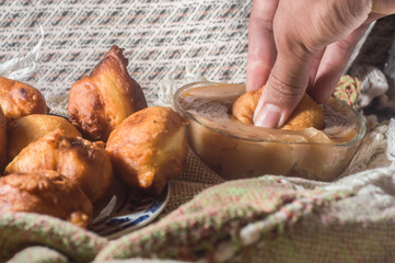 brazilian sweet called "bolinho de chuva" rain dumpling, or Fritter, in a natural home environment copy space and hands holding a dumpling, a pot with a milk candy on the side to accompany