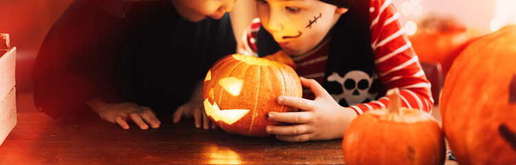 Girl in witch costume and boy in pirate costume looking into pumpkin
