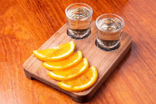 Two shots of mezcal with orange slices and worm salt on a wooden table with station for your text. Tequila shots. Mexican brandy concept.