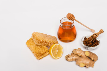 honey jar near wooden dipper, bowl with anise seeds, honeycomb, fresh lemon and ginger root on white