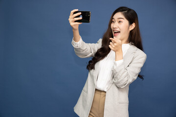 Young smiling cheerful Asian woman using social media on phone for video chatting isolated on deep blue background