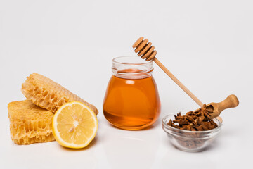 honeycomb, ginger root and fresh lemon, bowl with anise seeds and honey jar with wooden dipper on white