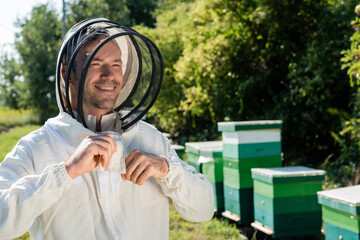 happy beekeeper adjusting protective suit on apiary