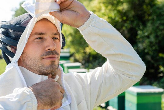 bee master taking off beekeeping suit on apiary - Powered by Adobe