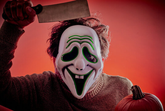 Scary Halloween man dressed in mask holding a knife and pumpkin.