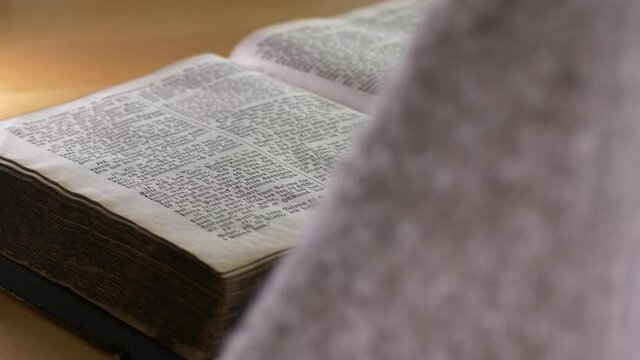 Close up rear shot of male hands touching bible, clasping hands in prayer. Static shot.
