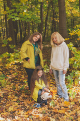 Naklejka na ściany i meble Portrait of three generations of happy beautiful women and dog looking at camera, hugging and smiling in autumn nature.