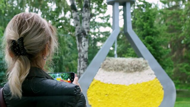 A blonde woman sends videos to her friends of beautiful travel destinations via the Internet. He shoots a video on a smartphone in a park, a flower bed with beautiful flowers.