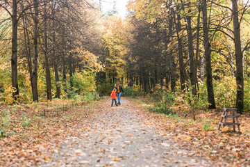 Mother and son walking in the fall park and enjoying the beautiful autumn nature. Season, single parent and children concept.