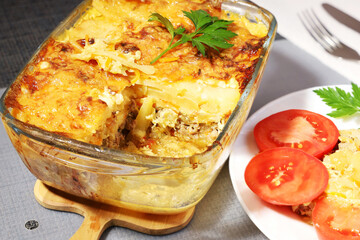 baked potatoes with meat in glass container, highlighted portion near dish with tomatoes