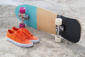 Orange sneakers next skateboard on concrete floor.