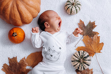 nursing baby infant in white clothes on a white background among pumpkins and autumn leaves