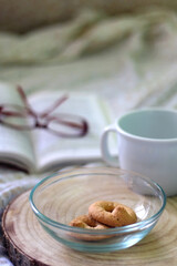 Bowl of cookies, cup, book and reading glasses on a bed. Selective focus.