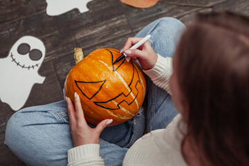 Woman painting pumpkin face and making pumpkin lantern for halloween sitting on wooden floor
