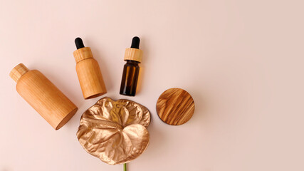 Cosmetics containers from wood lie around golden flamingo flower.Pastel background with copy...