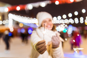 Fototapeta na wymiar Girl holding a sparkler in her hand. Outdoor winter city background, snow, snowflakes.