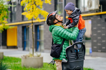 Naklejka premium Cute little boy with security helmet on the head sitting and his father take him from bike seat fooling around and play with son. Safe and child protection concept.