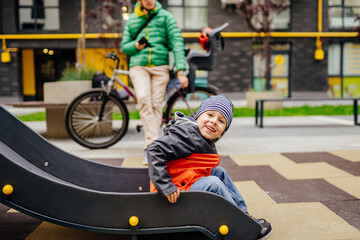 Little boy playing in the playground outdoor while his father standing and using smartphone on blurred background. Parent smartphone addiction children concept.