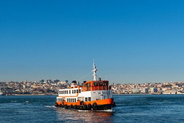 Fototapeta premium A traditional cacilheiro ferry boat crossing the Tagus River (Rio Tejo) with the city of Lisbon skyline on the background.
